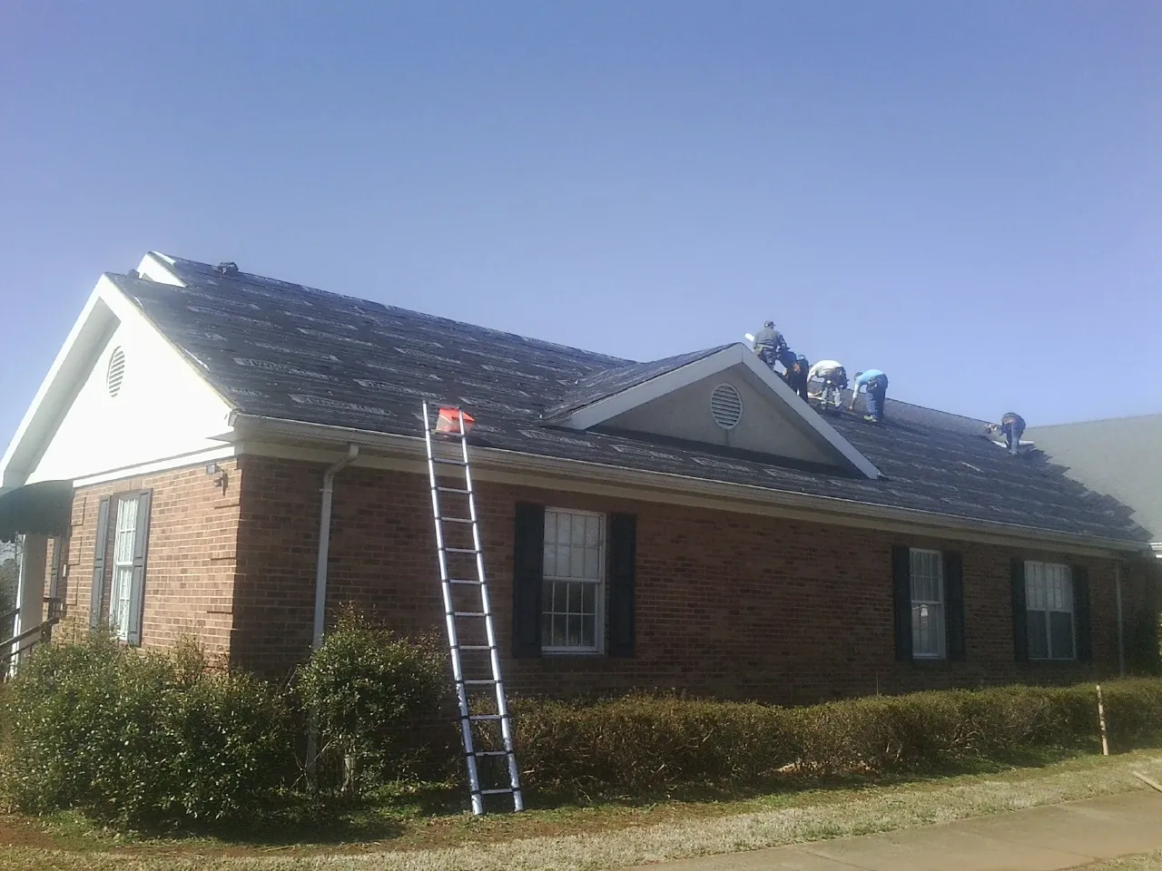Crew tearing shingles off a brick ranch roof with a ladder set — Emergency Roof Repair work by our crew in Waddy
