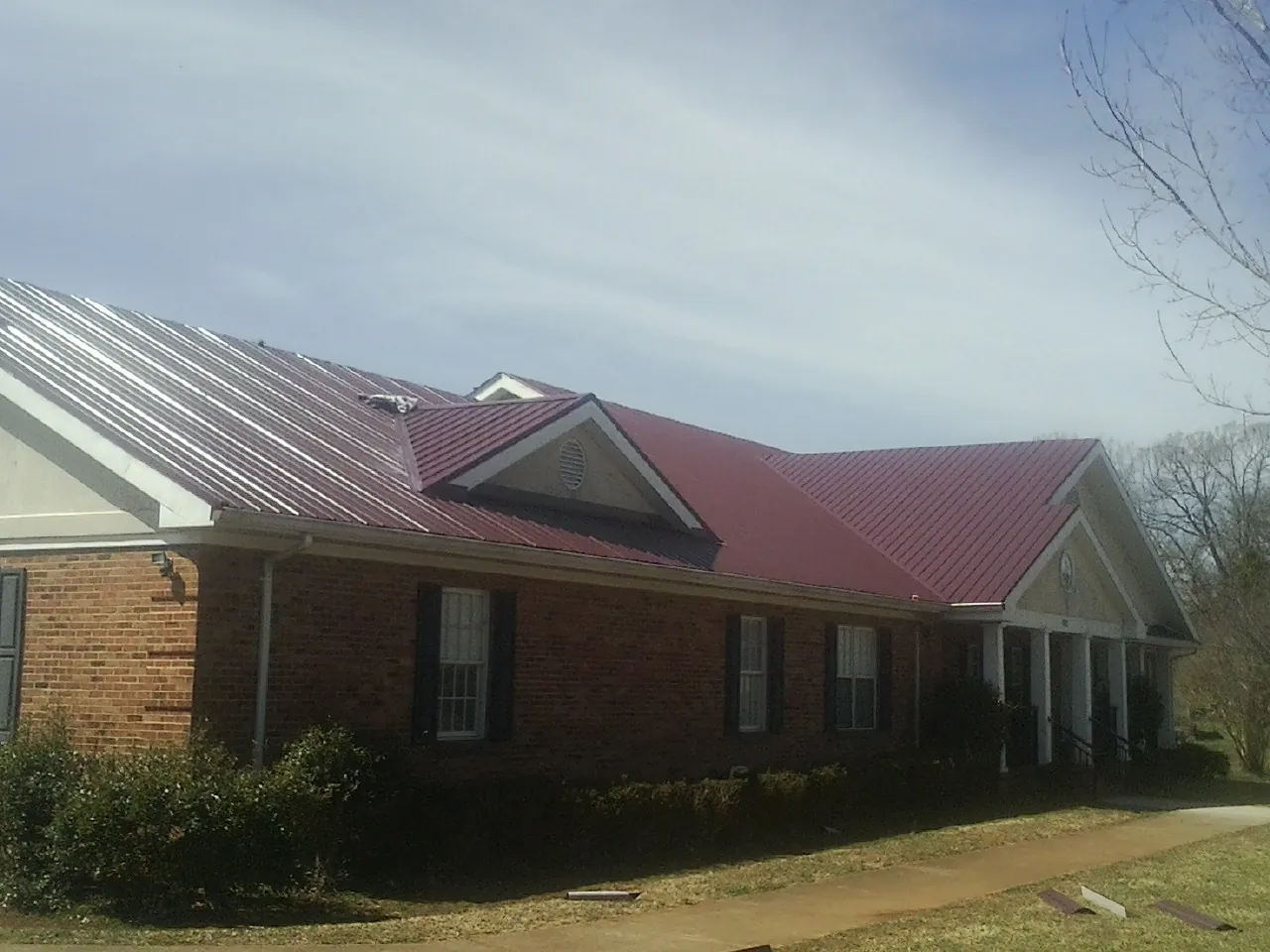Red metal roof with gabled entries on a long brick building, from a Hail Damage Roof Repair job in Waddy