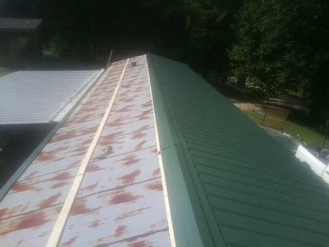 Old rusted panels beside newly installed green metal roofing — Wind Damage Roof Repair by Roofing Brothers in Waddy