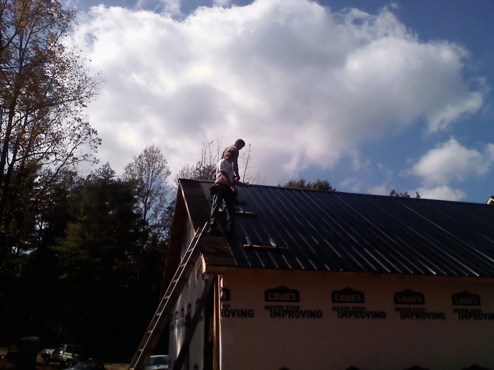 Roofer fastening dark metal panels high against a cloudy sky, from a Roof Inspection job in Waddy