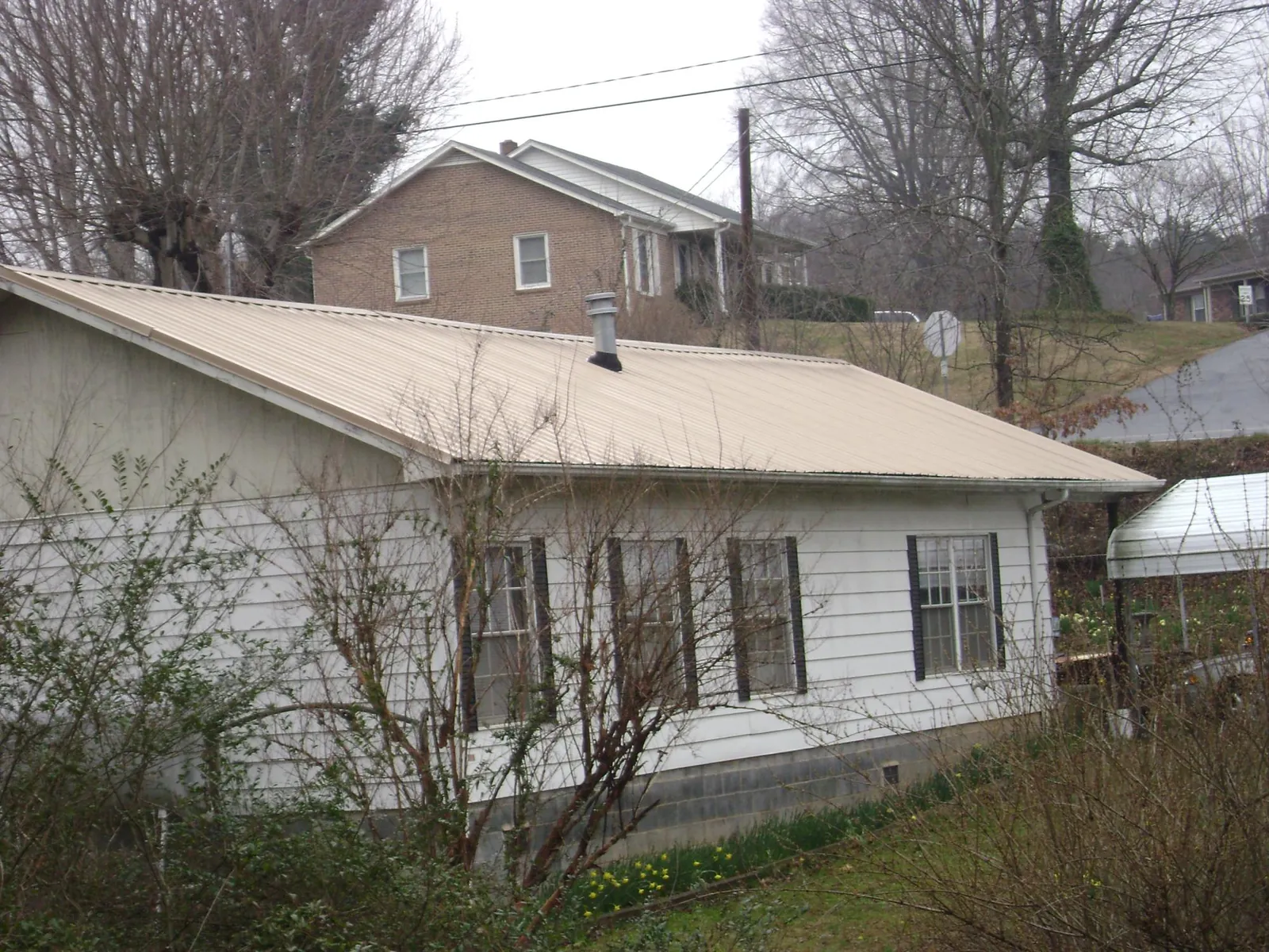 Tan metal roof on a white sided house set into a hillside — Commercial Roofing by Roofing Brothers in Waddy